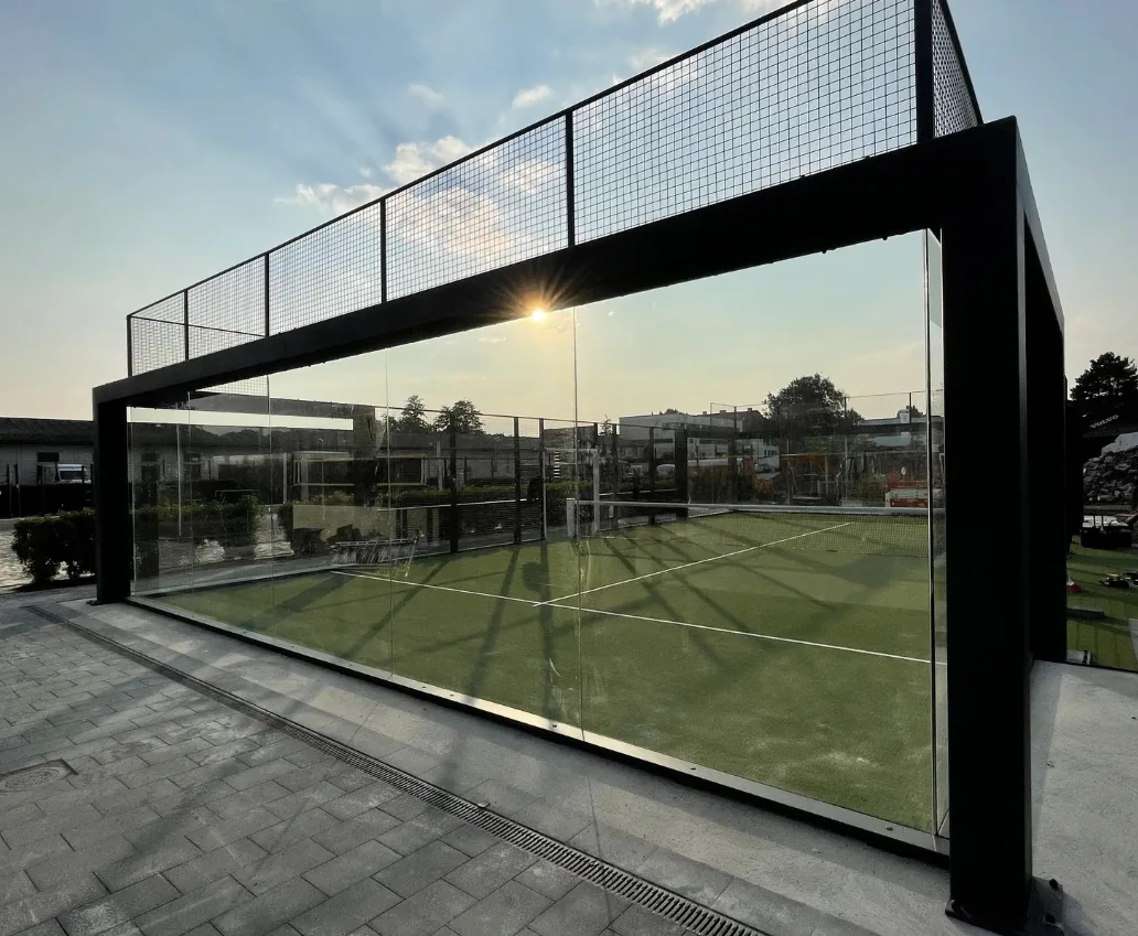 Architectural glass-walled padel court silhouetted at golden hour